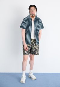 Short-sleeve striped shirt in blue and white, paired with floral-patterned shorts. Model wears white sneakers and white ankle socks.