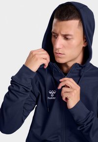 Donkerblauw hoodie met rits, gemaakt van een gladde stof, met een logo op de borst, een verstelbare trekkoord en aansluitende boorden.