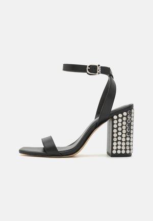 Black leather heeled sandals with an ankle strap. Features a square toe, smooth texture, and square block heel adorned with silver studs.