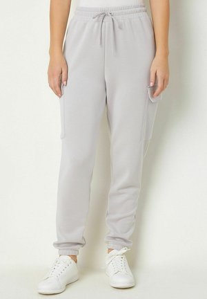Hellgraue Jogginghosen mit elastischem Bund; haben Seitentaschen und gerippte Bündchen; aus weichem, dehnbarem Stoff gefertigt. Kombiniert mit weißen Sneakers.