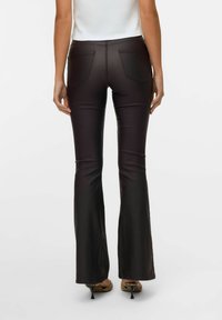 Pantalons évasés noirs avec une finition brillante, dotés de deux poches arrière et d'une texture lisse, associés à des chaussures à talons.