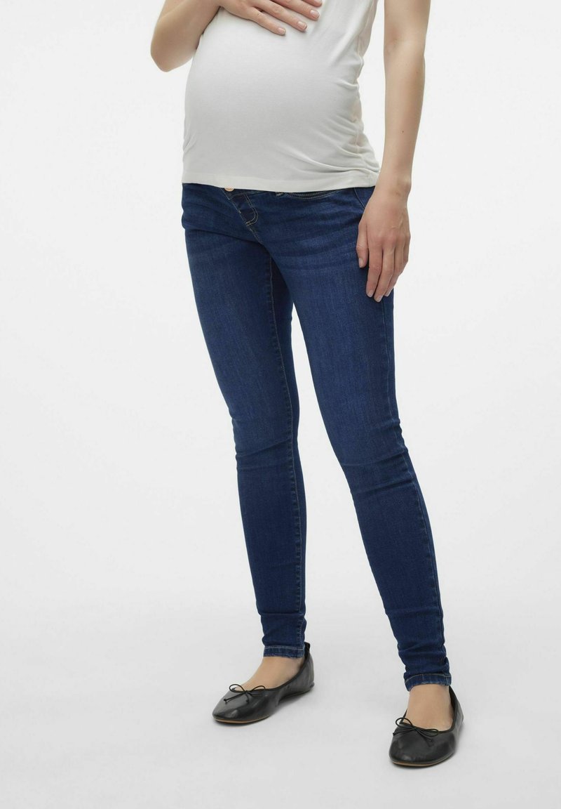 Jeans de maternidad de mezclilla en azul oscuro, con un corte ajustado, tejido elástico y una cinturilla estilizada que se adapta a una barriga en crecimiento.