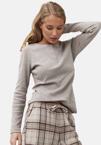 Camiseta de manga larga gris claro con cuello redondo y tapeta de cinco botones, combinada con pantalones de cuadros beige y marrón con cintura elástica.