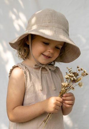 Young child wearing a beige sunhat and dress, smiling while holding a small bouquet of dried wildflowers.