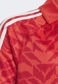 Röd tröja med ett lövmönster, med en klassisk krage och vita ränder längs axlarna. Tillverkad av slät, strukturerad tyg.