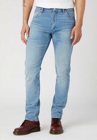 Jasnoniebieskie dżinsy o slim fit, z pięcioma kieszeniami i subtelnym wyblakłym efektem. Połączone z bordowymi butami ze sznurowadłami.
