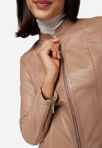Giacca di pelle rosa chiaro con un design aderente, colletto alto e chiusure a zip. Presenta dettagli a costine su spalle e polsini.