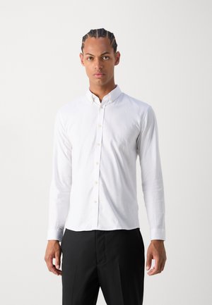 Camisa branca de manga longa feita de algodão, com colarinho abotoado e corte slim. Textura suave com um aspeto nítido.