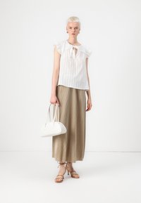 Blusa bianca a maniche corte con ruches e un nodo al collo, abbinata a una lunga gonna beige a coste e una borsa bianca. Sandali marroni con cinturini.