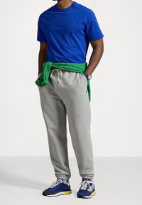 Královsky modrá košile s krátkým rukávem, šedé tepláky se stahovací šňůrkou, zelený svetr uvázaný v pase a modré sportovní boty se žlutými prvky.