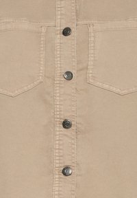 Chemise boutonnée couleur beige, avec boutons-pression métalliques, poches cousues, et une texture de tissu lisse. Col classique et coupe standard.