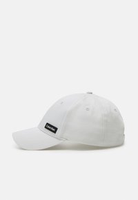 Cappellino da baseball in cotone bianco con visiera piatta, dotato di una patch nera con il logo Calvin Klein sul davanti e fori di ventilazione.