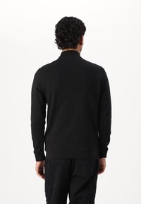 Maglione nero con collo alto, maniche lunghe e polsini a costine. Texture liscia, design semplice, senza motivi o dettagli visibili.