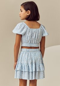 Világoskék két részes szett apró virágmintákkal, pöttyös ujjakkal és fodros szoknyával. Rugalmas derék és redőzött anyag a textúráért.