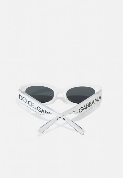 Lunettes de soleil blanches avec des verres teintés noirs, en forme d'œil de chat, dotées d'une monture transparente avec "DOLCE & GABBANA" imprimé sur les branches.