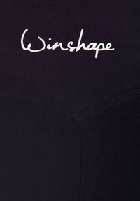Svarta leggings med V-formad sömdetalj, konturerad design och en vit "Winshape"-logotyp vid midjan. Slitstark, elastisk tyg.