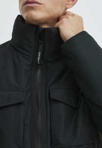 Chaqueta acolchada negra con cuello alto, cierre frontal de cremallera y dos bolsillos en el pecho. Tejido liso, resistente al agua y con detalles de costura mínimos.