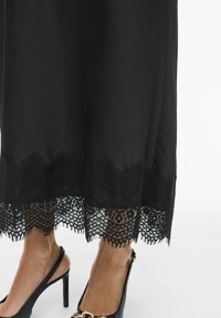 Črna obleka z čipkasto obrobo, okrašena s cvetličnimi vzorci na spodnjem robu. Oblečena s črnimi salonarji s peto, ki poudarjajo gladko teksturo tkanine.