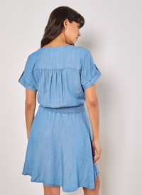 Vestido de mezclilla azul claro con mangas cortas enrolladas y cintura fruncida, que presenta un corte holgado y una falda en forma de A.