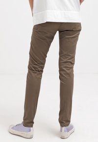 Brune slim-fit bukser lavet af glat stof, med lav talje. Sammen med lyse sneakers med reflekterende detalje på hælen.