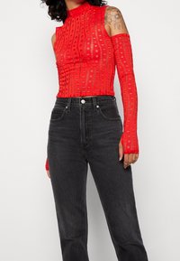 Top de punto rojo con mangas largas, con un cuello alto y diseño recortado. Combinado con jeans negros de talle alto.