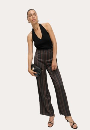 Woman wearing black halter top, brown and black vertical striped wide-leg pants, holding a black clutch, and wearing black strappy heels.