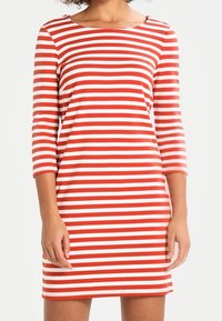 Czerwona i biała sukienka w paski, wykonana z elastycznego materiału, z dekoltem w łódkę i rękawami o długości 3/4, o dopasowanym kroju.