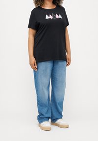 Svart bomull t-shirt med grafik av rosa och vita träd på framsidan, ihopparad med ljusblå vida jeans och vita sneakers.