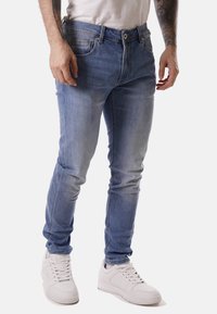 Jeans in denim azzurro chiaro con vestibilità slim, sbiadimento visibile e design standard a cinque tasche. Indossati con sneaker bianche e una t-shirt basic.