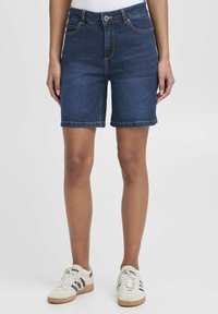 Mörkblå denimshorts med en åtsittande design, fem fickor och knappstängning. Klippta till knäslängd med sydda kanter.