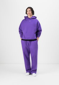 Lilla hettegenser med kengurulomme, kombinert med matchende joggebukser. Mykt stoff, avslappet passform og diskret logo-detall på brystet.