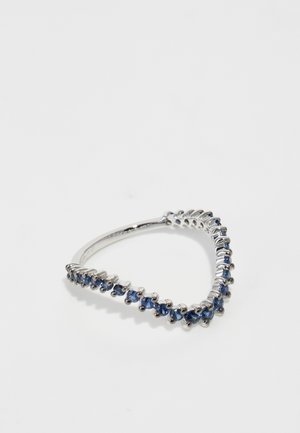 Anillo en tono plateado en forma de V decorado con piedras preciosas azules a lo largo de un lado, con una superficie lisa y pulida y bordes curvados.