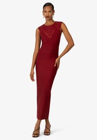 Rotes, figurbetontes Kleid mit ärmellosem Design, strukturiertem Oberteil und gerader Silhouette. Getragen mit schwarzen Riemchensandalen.