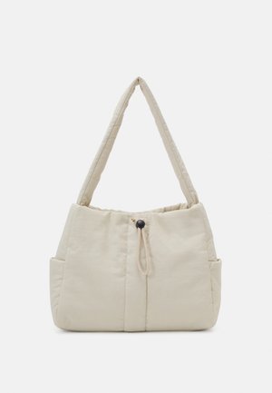 Beige padded shoulder bag with wide strap, elastic drawstring, and side pockets, displayed against a white background.