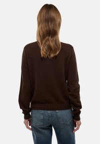 Pull en tricot marron à manches longues, avec des poignets et un ourlet côtelés, coupe décontractée, associé à un jean bleu taille haute.