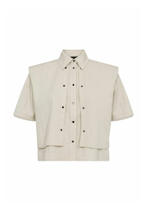 Kortærmet beige cropped skjorte med spids krave, der har knapper foran og store klapdetaljer på skuldrene.