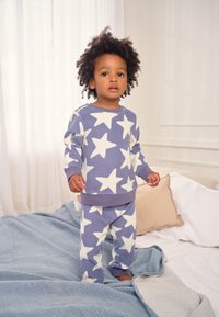 Lilla fleece pyjamasæt med hvide stjernemønstre, bestående af en langærmet top med rund hals og bukser med elastisk talje. Blød tekstur synlig.