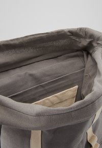 Hall hallitanud kangast kott, millel on pehme tekstuur, beezist puuvillast sangadega ja väike sisetasku. Avaus on lai ja struktuurita.