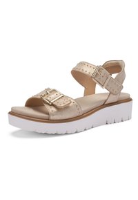 Sandale beige à bout ouvert avec deux brides cloutées ornées de boucles dorées et une semelle blanche épaisse à bande crantée.