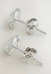 Pair of small silver stud earrings with butterfly clasps on a light surface.