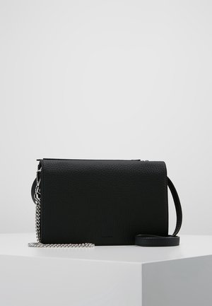 Bolso bandolera de cuero negro con textura, detalle de cadena plateada y correa ajustable, exhibido sobre una superficie blanca con fondo gris.