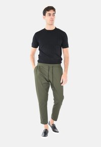 Maglietta nera a maniche corte a coste abbinata a pantaloni verde oliva con cordoncino e scarpe slip-on nere. Design semplice con vestibilità rilassata.