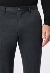 Ciemnoszare spodnie o dopasowanym kroju, wykonane z gładkiego materiału, z rozpięciem na jeden guzik i bocznymi kieszeniami, wyeksponowane na białym tle.