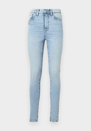 Jeans skinny de cor azul-claro feitos de denim, com cintura alta, cinco bolsos e padrões de desbotamento subtil. Fecho de zip com botão de metal.