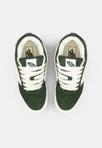 Zelene suedirane tenisice imaju bijelu gumenu đon, kremaste vezice i oznaku s Vans logotipom na jeziku.