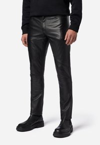 Schwarze Lederhosen mit schmaler Passform, glatter Textur, sichtbaren Nähten und einem mittelhohen Bund, kombiniert mit schwarzen Knöchelboots.