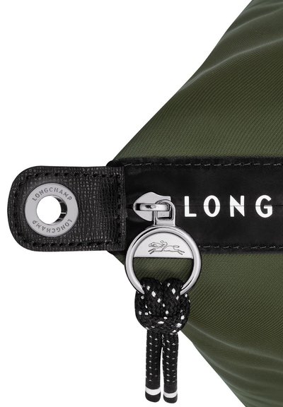 Olive green nylon bag corner with a black leather strap, silver hardware, embossed logo, and a knotted rope detail.