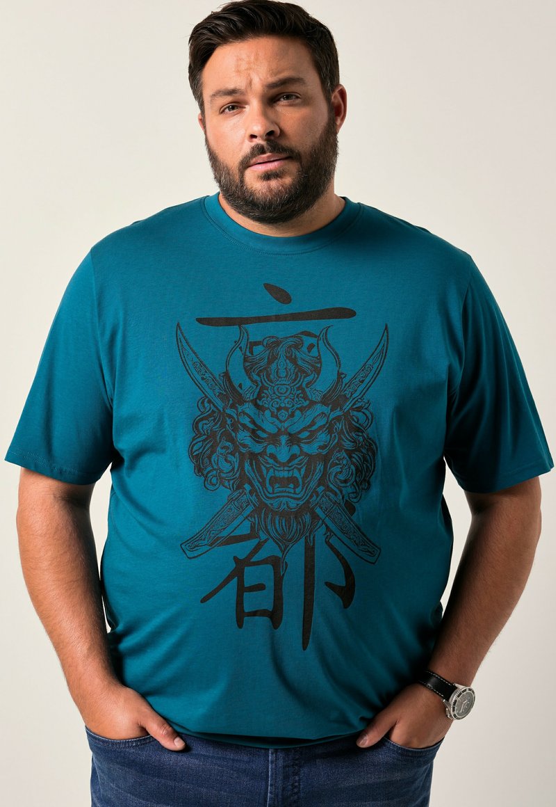 Camiseta de manga corta color azul verdoso con un diseño gráfico negro de una máscara feroz con espadas y texto, hecha de suave tela de algodón.