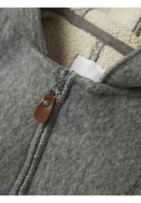 Hoodie zippé en polaire grise avec un intérieur doux et texturé, un tirette en cuir marron et des coutures contrastantes.