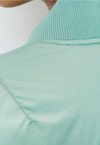 Sekce prošívané bundy ve světle mentolové zelené barvě s žebrovaným límcem a hladkým, lesklým povrchem s diagonálním prošíváním.